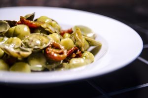 Primo piatto di gnocchi al pesto con vongole e pomodorini confit senza glutine